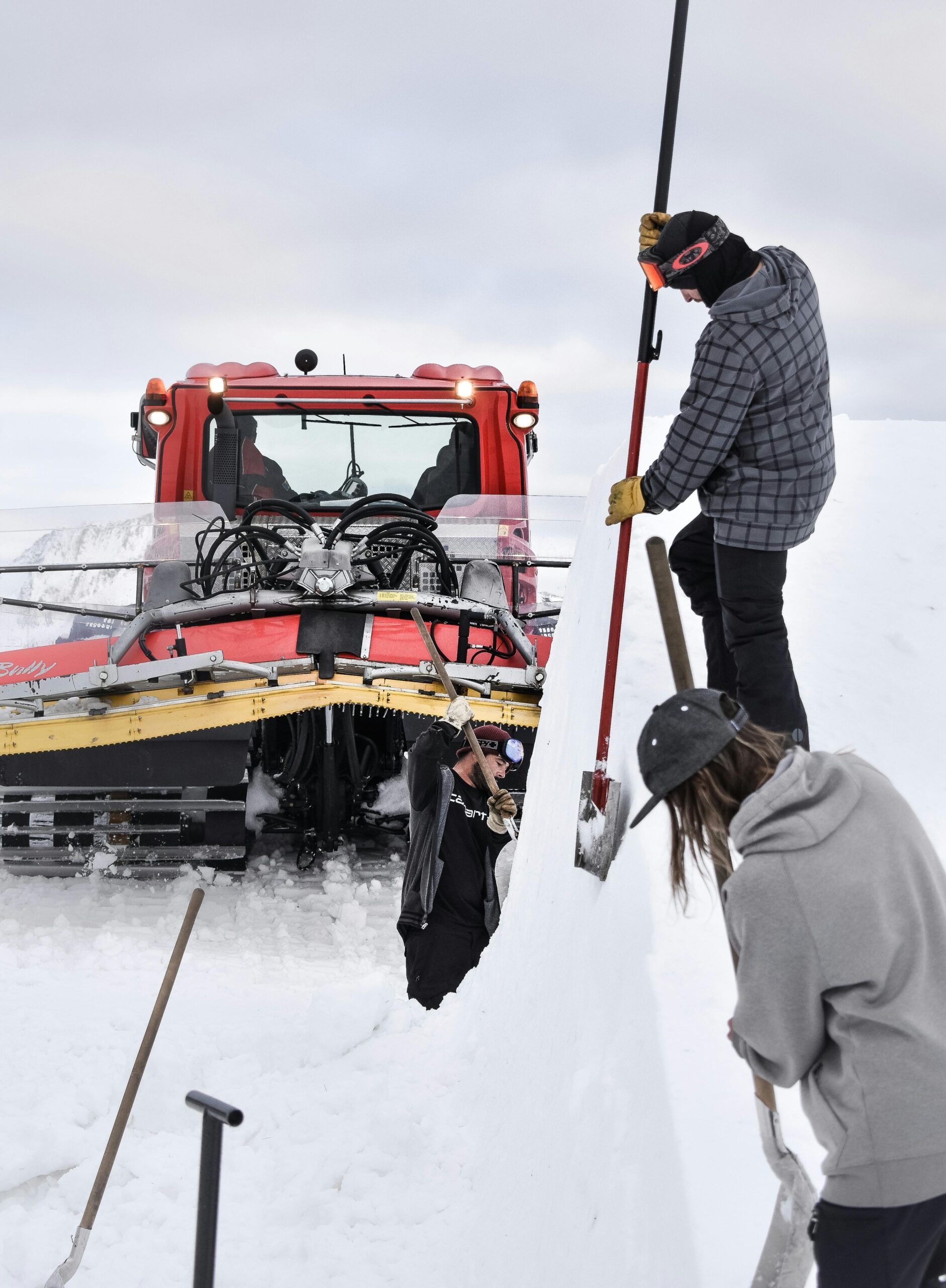 People clearing snow with shovels and a snowcat on a winter day.