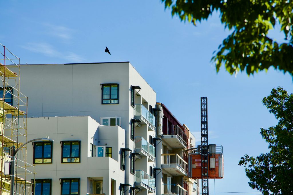 Modern building under construction with crane against clear blue sky and greenery.