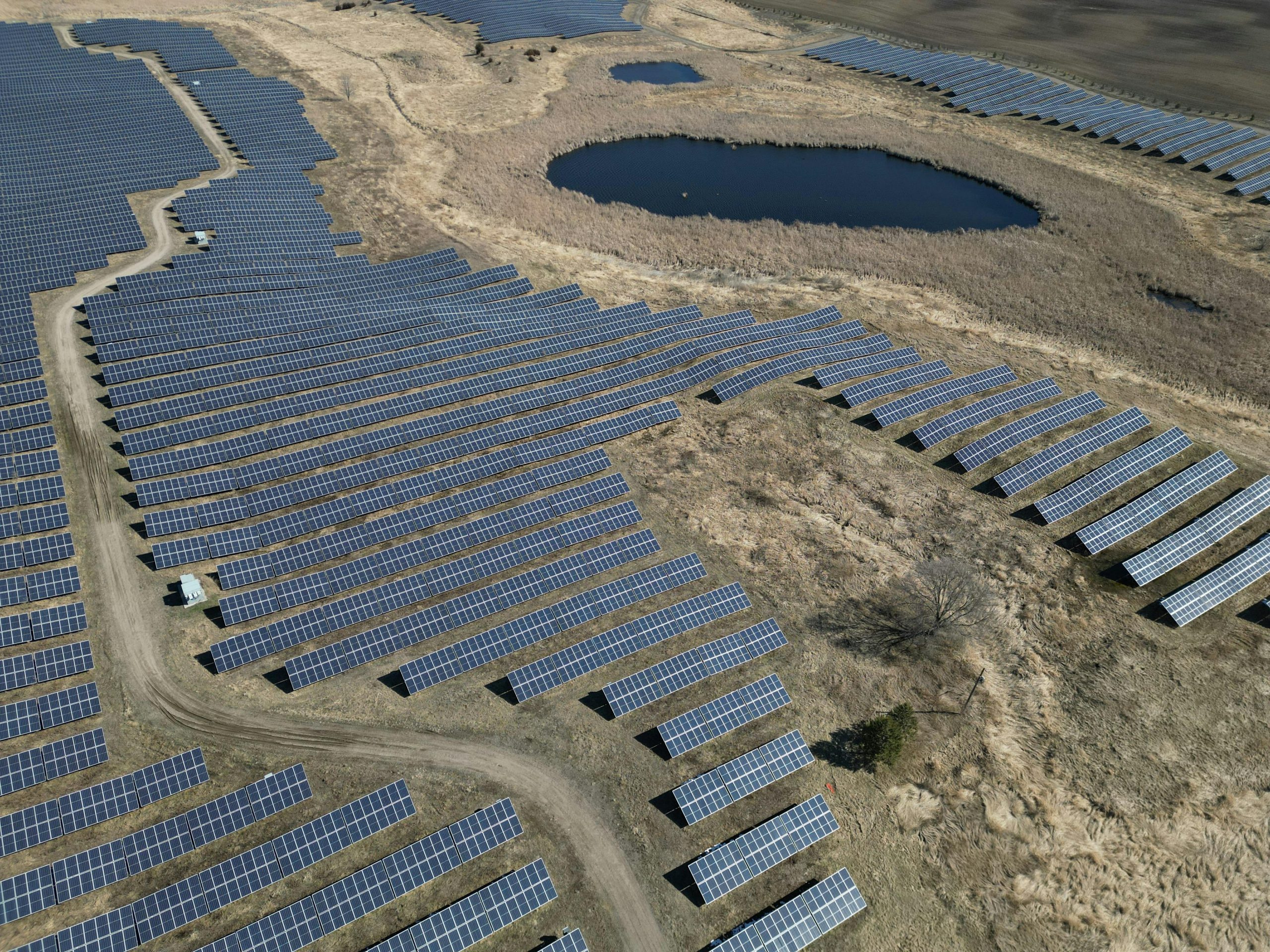 Expansive aerial view of a solar farm with rows of panels and a pond.